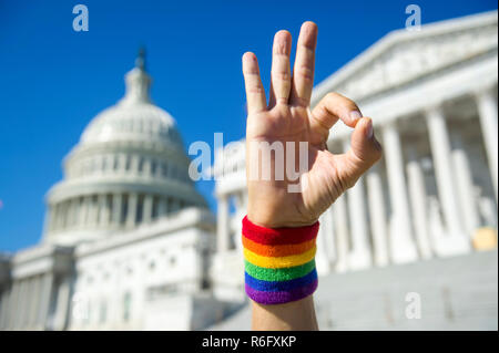 Mano che indossa il Gay Pride rainbow con la fascetta da polso rendendo okay gesto di fronte al Campidoglio di Washington DC, Stati Uniti d'America Foto Stock