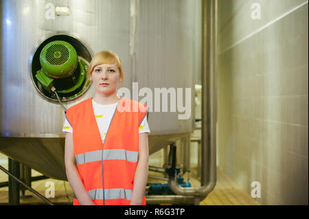 Lavoratore di sesso femminile che sulla fabbrica di birra. ritratto donna in accappatoio, permanente sulla linea di sfondo la produzione di cibo e di ispezione di controllo di gestione di apparecchiature per la produzione e la finitura di imbottigliamento prodotto utente finale acquirente Foto Stock