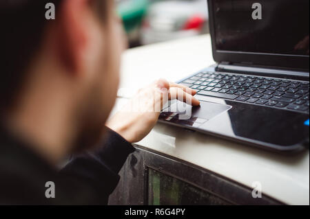 Uomo con notebook nel parcheggio nel cortile vicino a macchina sta facendo manipolazioni con cyber sistema, concetto Foto Stock