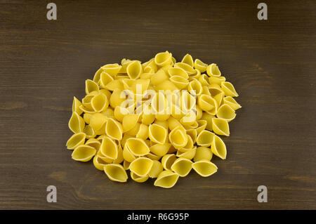 Conchiglie pasta di pelo scuro su uno sfondo di legno Foto Stock