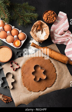 Gingerbread cookies preparazione. Pasta biscotto, cookie cutters, ingredienti su sfondo nero. Vista superiore Foto Stock