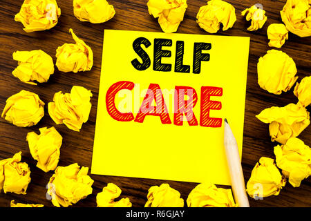 La scrittura di un testo che mostra Self Care. Il concetto di business per prendere la cura per la propria salute scritto su una nota adesiva carta, legno con sfondo giallo piegata la carta nel senso di pensare Foto Stock