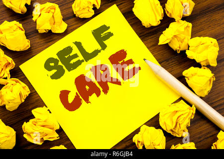 La parola, la scrittura Self Care. Il concetto di business per prendere la cura per la propria salute scritto su una nota adesiva carta, legno con sfondo giallo piegata la carta nel senso di pensare Foto Stock