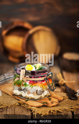 Tradizionale russo betroot stratificata e insalata di aringa (sotto una pelliccia) in un barattolo di vetro, legno rustico sfondo, il fuoco selettivo Foto Stock