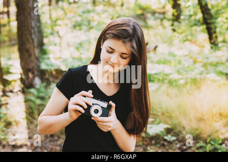 Felice i Capelli rossi ragazza caucasica giovane ragazza adolescente, adolescente fotografo fotografare il vecchio Retro Vintage fotocamera a pellicola in estate foresta verde. Gi Foto Stock