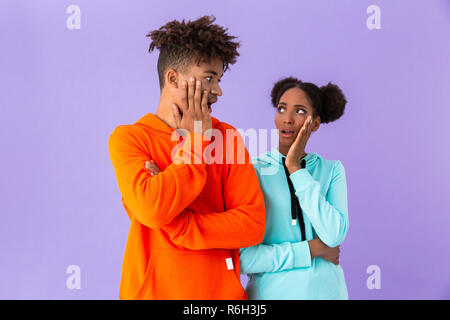 Foto di sorpresa americano africano del fratello e sorella urlando e toccando la faccia isolate su sfondo viola Foto Stock