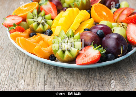 Un assortimento di frutti e bacche platter, fragole mirtilli, mango orange, Apple, uva da tavola, kiwi sul grigio Sfondo legno, fuoco selettivo Foto Stock