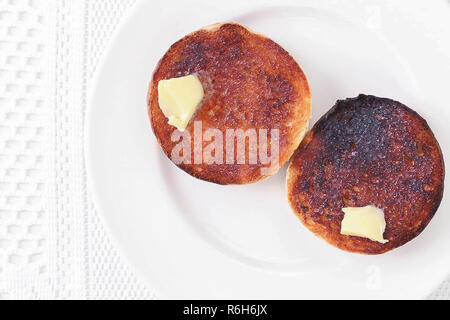 Bruciò muffin, tostata servita su una piastra bianca con burro su sfondo bianco, Birds Eye view. Foto Stock