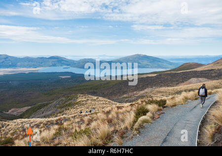 Giovane bella donna che cammina verso il basso il percorso di origine vulcanica con lago Taupo della distanza sul Tongariro Crossing Foto Stock