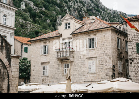 La facciata di un ordinario vecchio edificio con finestre e un balcone in Montenegro. Alloggiamento tradizionali. In fondo è una montagna. Per l' edificio è la bandiera del Montenegro. Foto Stock