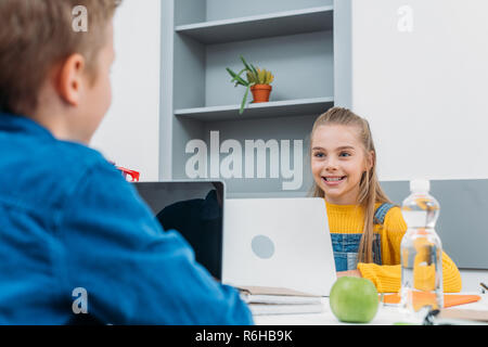 La scolaretta sorridente e schoolboy seduto alla scrivania, utilizzando i notebook e apprendimento in aula Foto Stock