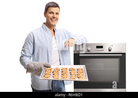 Giovane uomo tenendo un vassoio di biscotti appena sfornati e appoggiate su un forno isolato su sfondo bianco Foto Stock