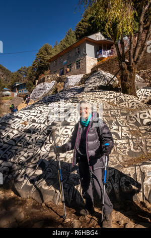 Il Nepal, Benkar, senior trekker un enorme dipinto e scolpito mani buddista pietra sul Campo Base Everest Trek percorso Foto Stock