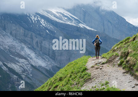 Giovane bella donna in piedi su un sentiero di montagna che guarda oltre la gamma nelle alpi svizzere Foto Stock