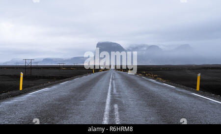 Una strada che conduce attraverso il nero levigato panorama verso Misty Mountains in Islanda Foto Stock