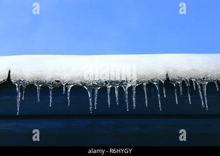 Ghiaccioli che pendono verso il basso da sotto il tetto della casa. Congelati modello invernale Foto Stock