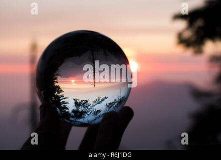 Tramonto sulla California's Sierra Nevada con Sun e creste sull orizzonte e alberi in silhouette. Catturato nel globo di vetro la riflessione. Foto Stock