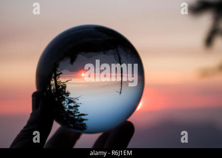 Tramonto sulla California's Sierra Nevada con Sun e creste sull orizzonte e alberi in silhouette. Catturato nel globo di vetro la riflessione. Foto Stock