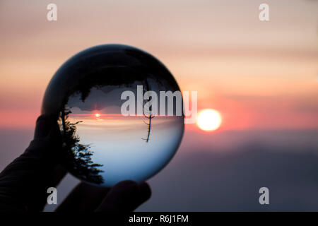 Tramonto sulla California's Sierra Nevada con Sun e creste sull orizzonte e alberi in silhouette. Catturato nel globo di vetro la riflessione. Foto Stock
