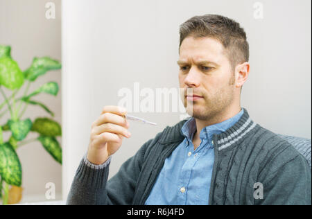 Triste uomo bello guardando il termometro. Foto Stock