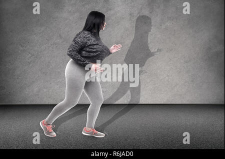 Plus-dimensionato donna corre per la sua sottile ombra sul muro, il concetto di perdita di peso Foto Stock