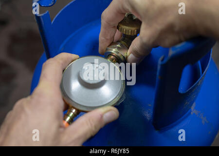 Regolatore per propan-butano bombola del gas e accessori su un workshop in legno tavolo. Accessori per gas in officina. Sfondo scuro. Foto Stock