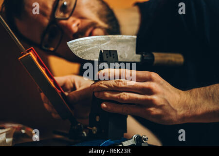 Uomo caucasico affilatura di un giapponese coltello da cucina con un moderno dispositivo whetstone Foto Stock