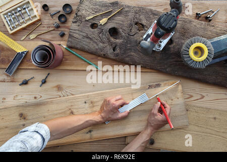 Falegname mani lavorano il legno, misurando con metro e matita vecchio rustiche tavole in legno, vista superiore con strumenti in background Foto Stock