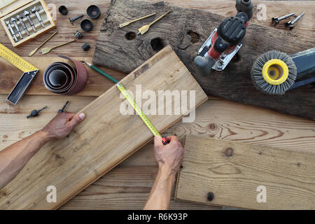 Falegname mani lavorano il legno, misurando con il metro a nastro vecchio rustiche tavole in legno, vista superiore con strumenti in background Foto Stock