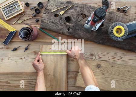 Falegname mani lavorano il legno, misurando con il metro a nastro vecchio rustiche tavole in legno, vista superiore con strumenti in background Foto Stock