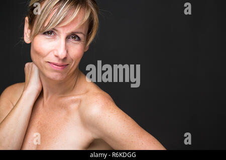 Ritratto di un sorridente di mezza età donna caucasica contro uno sfondo scuro - irradiando la fiducia e la femminilità (SHALLOW DOF dai toni di colore immagine) Foto Stock