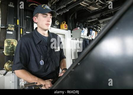 Pacifico occidentale (22 maggio 2017) marinaio Juan Molina, da Austin, Texas, mans timone di Ticonderoga-class guidato-missili cruiser USS Lake Champlain (CG 57). Gli Stati Uniti Marina ha pattugliato il Indo-Asia-Pacifico di routine per più di 70 anni regionale di promozione della pace e della sicurezza. Foto Stock