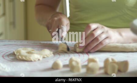 La donna è la fase di tranciatura di un impasto con un coltello per la produzione di gnocchi di patate con formaggio, 4K close-up Foto Stock