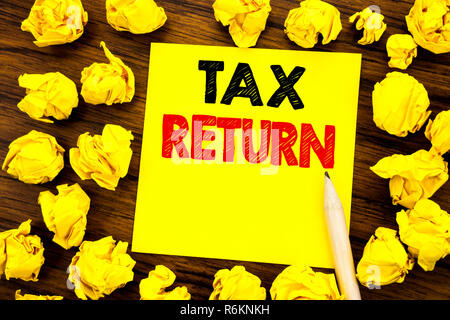 La scrittura di un testo che mostra il ritorno fiscale. Il concetto di business per la Fiscalità rimborso scritto su una nota adesiva carta, legno con sfondo giallo piegata la carta nel senso di pensare Foto Stock