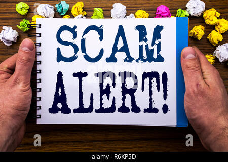 La scrittura di un testo che mostra Scam Alert. Il concetto di business per Avviso di frode scritto sul notebook notepad libro sul legno in legno con uno sfondo imprenditore man mano e dito. Foto Stock