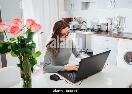 Donna al lavoro su laptop in cucina moderna. Giovani stanchi freelancer digitando Foto Stock