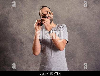 Giovane uomo barbuto ceaning i suoi occhiali Foto Stock