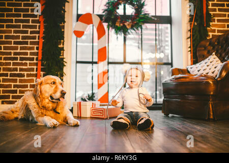 Amicizia uomo bambino e cane pet. Tema Natale Capodanno Vacanze invernali. Bimbo gattona impara a piedi con pavimento in legno e decorata interno di casa e migliore amico cane di razza Labrador golden retriever Foto Stock