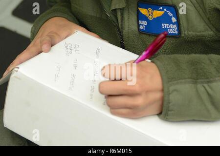 Petty Officer 2a classe Mandi Stevens aviazione un tecnico di manutenzione dalla guardia costiera Stazione aria Barbieri punto, scrive una nota per essere posto all'interno del lungo raggio dispiegabile kit di discesa ad un recipiente di disabili circa 80 miglia fuori della Tonga Maggio 25, 2017. Gli Stati Uniti Coast Guard ha lavorato con RCC in Nuova Zelanda e Tonga per effettuare il salvataggio di sei pescatori a bordo di un 40-piede nave in ritardo su un viaggio da Tonumeia isola di Tongatapu. Foto Stock