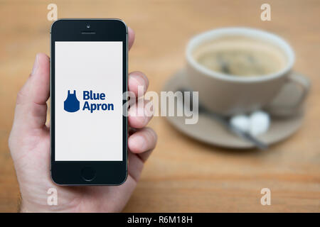 Un uomo guarda al suo iPhone che visualizza il grembiule blu logo (solo uso editoriale). Foto Stock