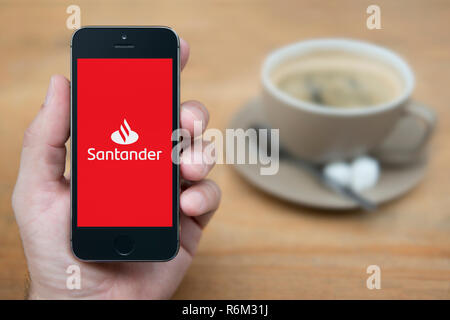 Un uomo guarda al suo iPhone che visualizza la banca Santander logo (solo uso editoriale). Foto Stock