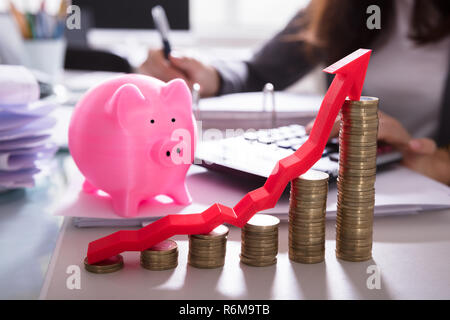 Monete impilate e la freccia nella parte anteriore del Piggybank Foto Stock