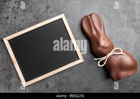 Il cioccolato coniglietto di Pasqua e lavagna vuota su sfondo rustico Foto Stock