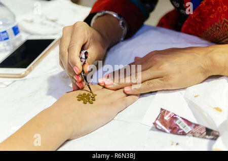 Una donna indiana si applica un Mehndi design per una mano della ragazza con un cono di henné, nov. 17, 2018 al Mobile Festival Internazionale di Mobile, Alabama. Foto Stock