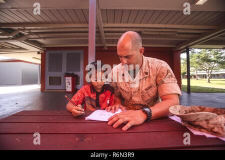 DARWIN Australia - STATI UNITI Il personale marino Sgt. Il Bret Daneker, plotone sergente, azienda I, 3° Battaglione, 4° Reggimento Marini, 1° Divisione Marine, Marine forza rotazionale di Darwin, tutor un bambino con la sua grammatica lavoro scuola durante un evento di volontariato, 31 maggio 2017. Lo stesso gruppo di Marines continuerà la visita e guida gli studenti durante tutto il loro tempo in Darwin. I marines si sono impegnati a servire la comunità locale e continuerà ad avere un impatto quando disponibile. Foto Stock