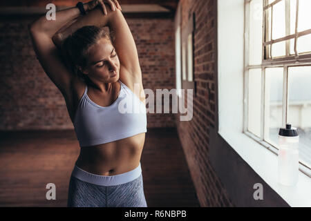 Montare la donna in abbigliamento sportivo facendo esercizi di stretching in palestra vicino alla finestra. Femmina in fase di riscaldamento per allenamento in palestra. Foto Stock