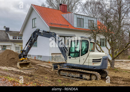 FLODA, Svezia - 21 novembre 2018: piccolo escavatore paesaggio facendo lavorare nel giardino di casa indipendente Foto Stock