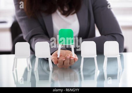 Imprenditrice scegliendo sedia verde tra le sedie bianche in una riga Foto Stock