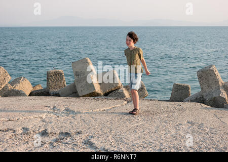 Ragazzo su uno sfondo del mare e del sole strizzare gli occhi contro il vento. Foto Stock