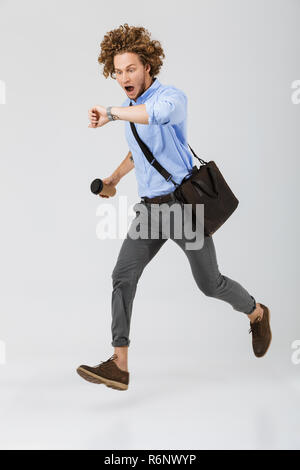 Lunghezza completa di un giovane imprenditore in ritardo isolate su sfondo bianco, tenendo takeaway tazza da caffè, borsa, guardando un orologio da polso Foto Stock